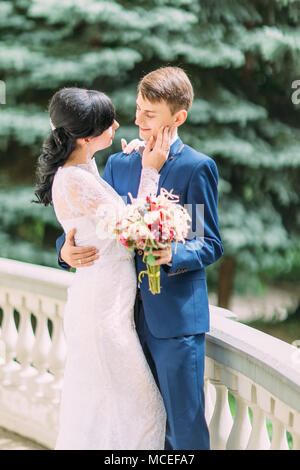 La mezza lunghezza sensibile ritratto dell'avvolgente sposi novelli. La sposa è accarezzare la guancia dello sposo. Foto Stock