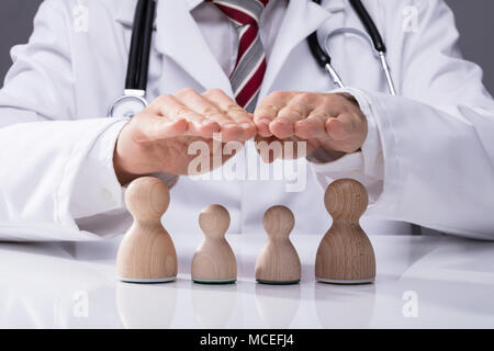 Close-up di un medico a mano in legno di protezione famiglia sulla scrivania Foto Stock