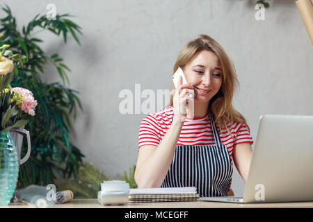 Immagine di un fioraio donna parlando al telefono mentre è seduto a tavola con il computer Foto Stock