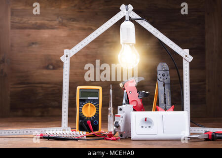Strumenti di riparazione sotto la casa illuminata realizzata con nastro di misurazione sul tavolo di legno Foto Stock