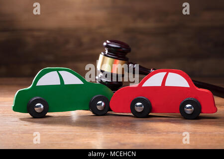 Collisione del legno e di due automobili giocattolo nella parte anteriore del martello sul tavolo di legno Foto Stock