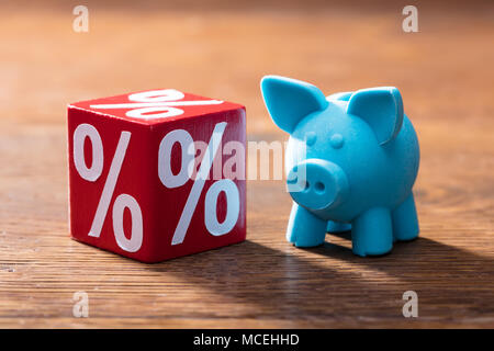 Close-up di simbolo di percentuale sul blocco rosso e blu Piggybank sul tavolo di legno Foto Stock