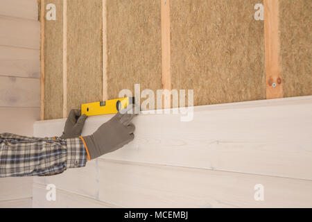 Il lavoratore fa opere di finitura delle pareti con un bianco tavola di legno, utilizzando una linea laser livello. Costruzione di isolante termico eco-telaio in legno casa con legno piastre in fibra Foto Stock