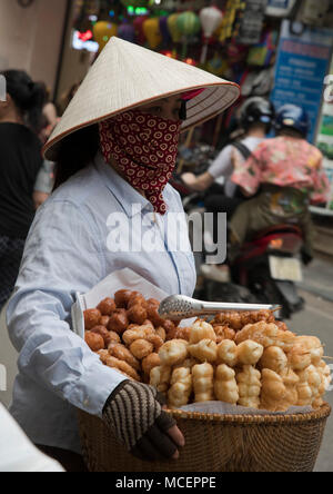 Un vietnamita donna che indossa un cappello conico vendita di pasticceria da un cestello nel quartiere vecchio, Hanoi, Vietnam, sud-est asiatico Foto Stock