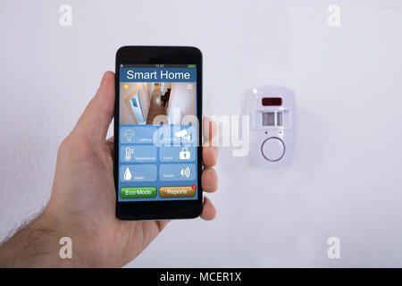 Mano umana utilizzando il telefono cellulare nella parte anteriore del sistema di protezione montato sulla parete Foto Stock