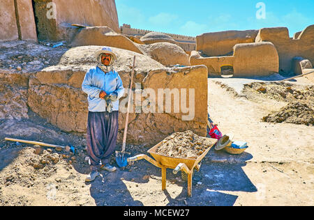 RAYEN, IRAN - 16 ottobre 2017: Il lavoratore sorridente del Dipartimento di Restauro di Arg-e Rayen sito archeologico pone con i suoi strumenti - la pala e whee Foto Stock