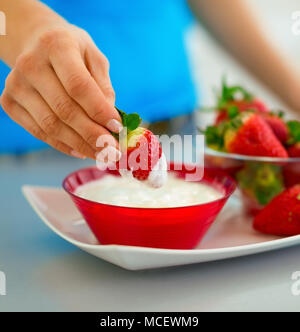 Primo piano sulla felice giovane donna di mangiare fragole con yogurt in cucina Foto Stock