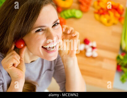Sorridente giovane donna con pomodori ciliegia come orecchini Foto Stock