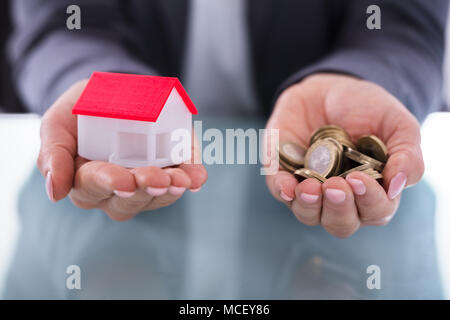 Close-up di un imprenditore la mano che trattiene le monete e modello di casa Foto Stock