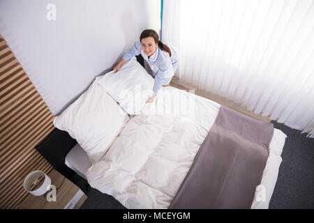 Felice governante femmina disponendo dei cuscini sul letto in camera di albergo Foto Stock