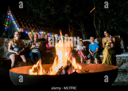 Famiglia avente un barbecue party seduti davanti al fuoco Foto Stock
