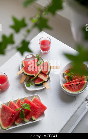 Fresco frullato di rosso in un bicchiere con pezzi tagliati a fette di cocomero sul tavolo. Foto Stock