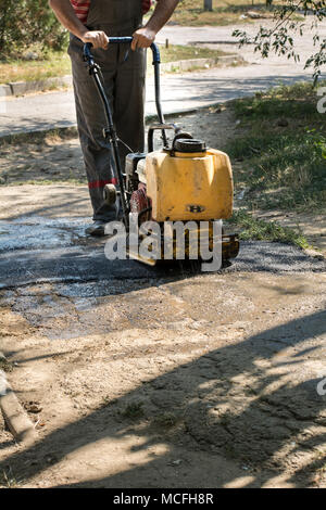 Strada di dettagli della riparazione. Un lavoratore con un manuale lastricatore allinea l'asfalto caldo sulla strada. Foto Stock