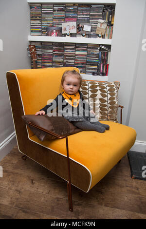 bambino di 11 mesi seduto su una grande poltrona arancione Foto Stock