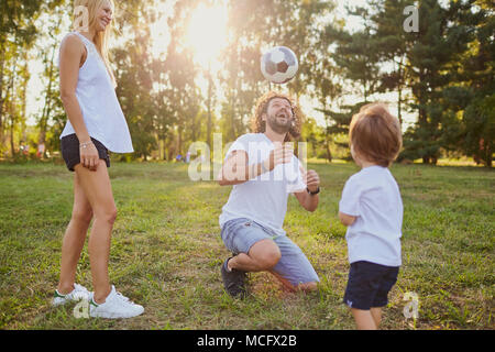 La famiglia gioca con una palla nel parco. I genitori con figlio di erba in natura. Foto Stock