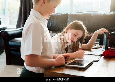 Little Boy e sua sorella stanno studiando insieme a casa. Entrambi hanno una tavoletta digitale e la ragazza è iscritto in un planner. Foto Stock