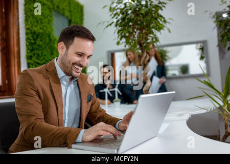 Giovani bel successo imprenditore sorridente analizzando i piani del grafico che mostra il successo, e lavorando sul computer portatile in ufficio. Foto Stock