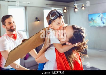 La famiglia felice in costumi di supereroi giocando insieme in una stanza. Foto Stock