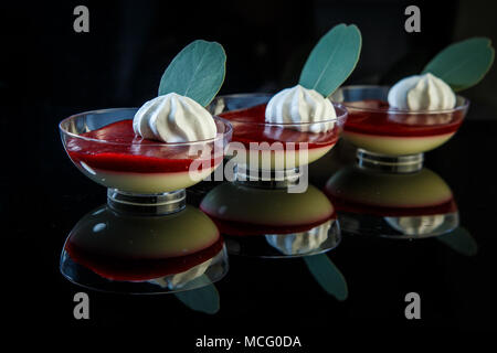 Blackberry panakota dessert decorate con la panna e le erbe in ciotole in vetro nero su sfondo a specchio Foto Stock