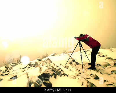 Effetto astratto. Fotografo di viaggio facendo le foto in antiche pietre sulla cima innevata della montagna. Inverno freddo e nebbiosa mattina in montagna Foto Stock