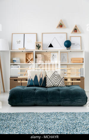 Semplice soggiorno interno con futon verde invece di un divano e poster su scaffali contro il muro bianco Foto Stock