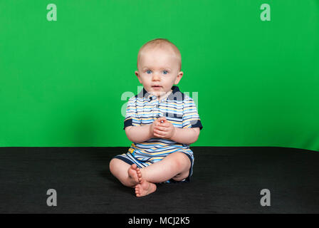 10 Mesi Happy Baby Boy su uno sfondo verde a giocare con le mani Foto Stock