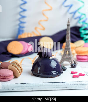 Lilla torta rotonda con macarons su un bianco tavola di legno, dietro una carta multicolore serpentina Foto Stock