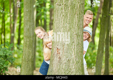 La famiglia felice è di giocare a nascondino dietro gli alberi della foresta in estate Foto Stock