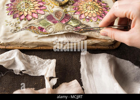 Studio di restauro, restauratore, controlli a mano artisticamente ricamato panno di seta strappato aperto con le pinzette, Monaco di Baviera, Germania Foto Stock