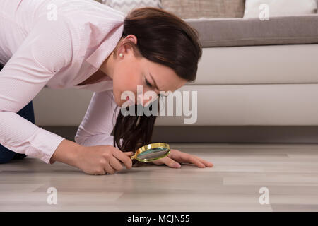 Vista laterale di una giovane donna che guarda al pavimento di legno attraverso la lente di ingrandimento Foto Stock