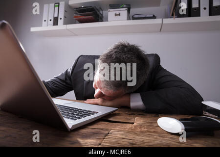 Imprenditore dormire in ufficio con laptop sulla scrivania in legno Foto Stock