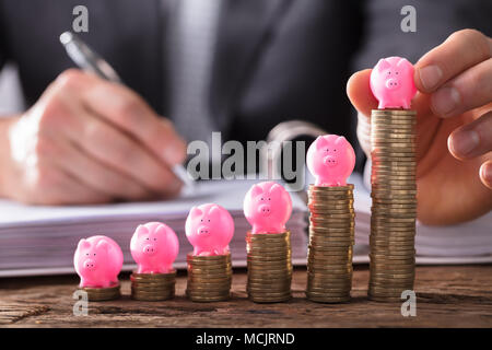 Close-up di un imprenditore la mano collocando Piggybank sulle monete impilate su scrivania in legno Foto Stock