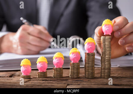 Close-up di un imprenditore la mano collocando Piggybank con elmetto sulla crescente monete impilate Foto Stock