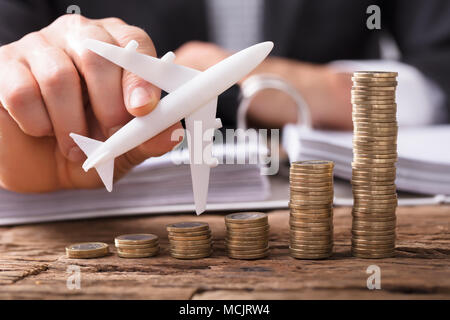 Close-up di un imprenditore la mano Battenti aereo su monete impilate a Workplace Foto Stock