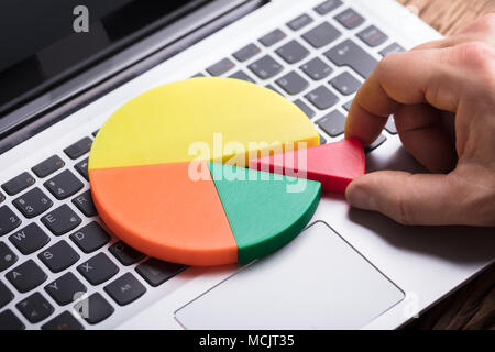 Close-up di una mano umana ponendo ultimo pezzo nel grafico a torta sulla tastiera del notebook Foto Stock