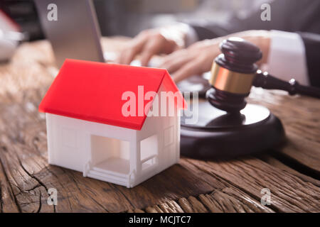 Close-up del modello di casa con il Tetto rosso e martello sulla scrivania di legno nelle aule di tribunale Foto Stock