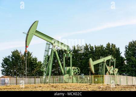 Due pumpjacks attiva il pompaggio di olio al di fuori di un ben posizionato nel centro della Francia sotto un cielo blu. Foto Stock