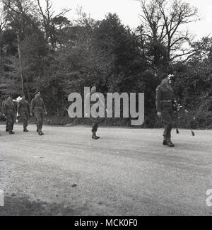 1955, Bucks, Inghilterra, un piper conduce una truppa di soldati britannici lungo una via in una foresta su una formazione marzo, Foto Stock