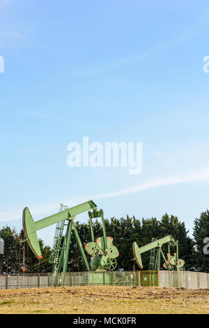 Due pumpjacks attiva il pompaggio di olio al di fuori di un ben posizionato nel centro della Francia sotto un cielo blu. Foto Stock