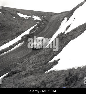 Degli anni Cinquanta, storico, automobile parcheggiata su uno spiovente di valley road accanto a parzialmente coperta di neve colline, Gran Bretagna. Foto Stock
