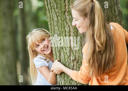 Ragazza bionda di giocare a nascondino nel bosco insieme con la madre Foto Stock