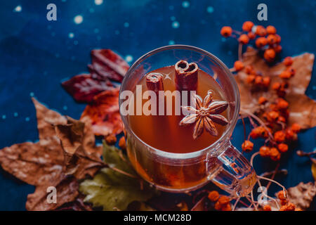 Il tè con la cannella in un autunno ancora in vita con caduta foglie e bacche di cenere sul bagnato sullo sfondo di legno. Concetto di stagione con copia spazio. Foto Stock
