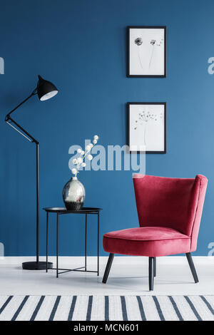 Sedia rossa accanto al tavolo con fiori e lampada in blu soggiorno interno con poster Foto Stock