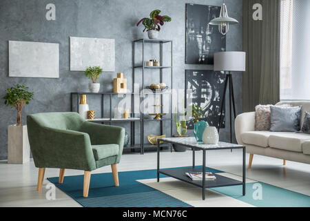 Poltrona verde accanto a un tavolo in metallo con pattern di marmo posta in campo industriale living room interior con piante e decorazioni Foto Stock