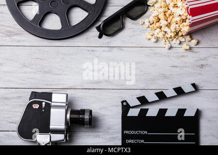 Vista in elevazione della fuoriuscita di popcorn con Clapperboard, occhiali 3d, bobina di pellicola e macchina fotografica del film Foto Stock