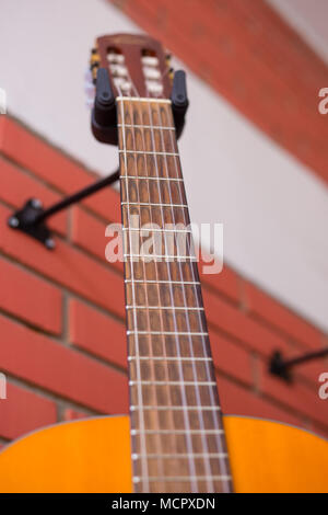 Chitarra elettrica in legno appesa su un gancio davanti alla parete bianca  Foto stock - Alamy