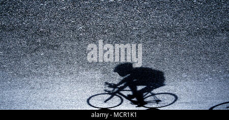 Sfocata silhouette e ombra di un ciclista professionista in bianco e nero sulla strada asfaltata nella notte Foto Stock