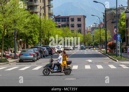 Un giovane cinese paio ride su uno scooter a motore. La bambina indossa un abito giallo e giostre pillion seduta sella laterale. Tonglu, nella provincia di Zhejiang, in Cina. Foto Stock