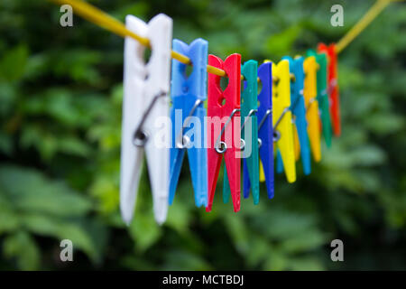 Clothespins colorati appesi a un stendibiancheria. Sullo sfondo sono gli alberi. Foto Stock