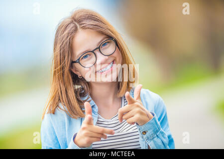 Ritratto di felice smilling teenage ragazza giovane con gli occhiali e il bel sorriso che mostra con entusiasmo a voi. Foto Stock